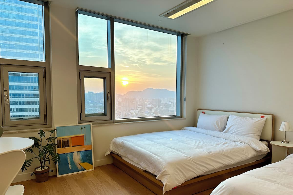 Une chambre d’hôtel avec un lit, un bureau, une chaise, une plante en pot et un tableau.
