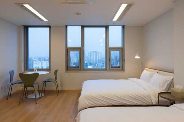A modern hotel room with a large bed, a round table with chairs, and three large windows offering a city view. - Maxtyle Guesthouse Dongdaemun (Seoul)