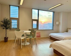 A hotel room with a bed, a dining table with chairs, a potted plant, and large windows with a cityscape view. - Maxtyle Guesthouse Dongdaemun (Seoul)