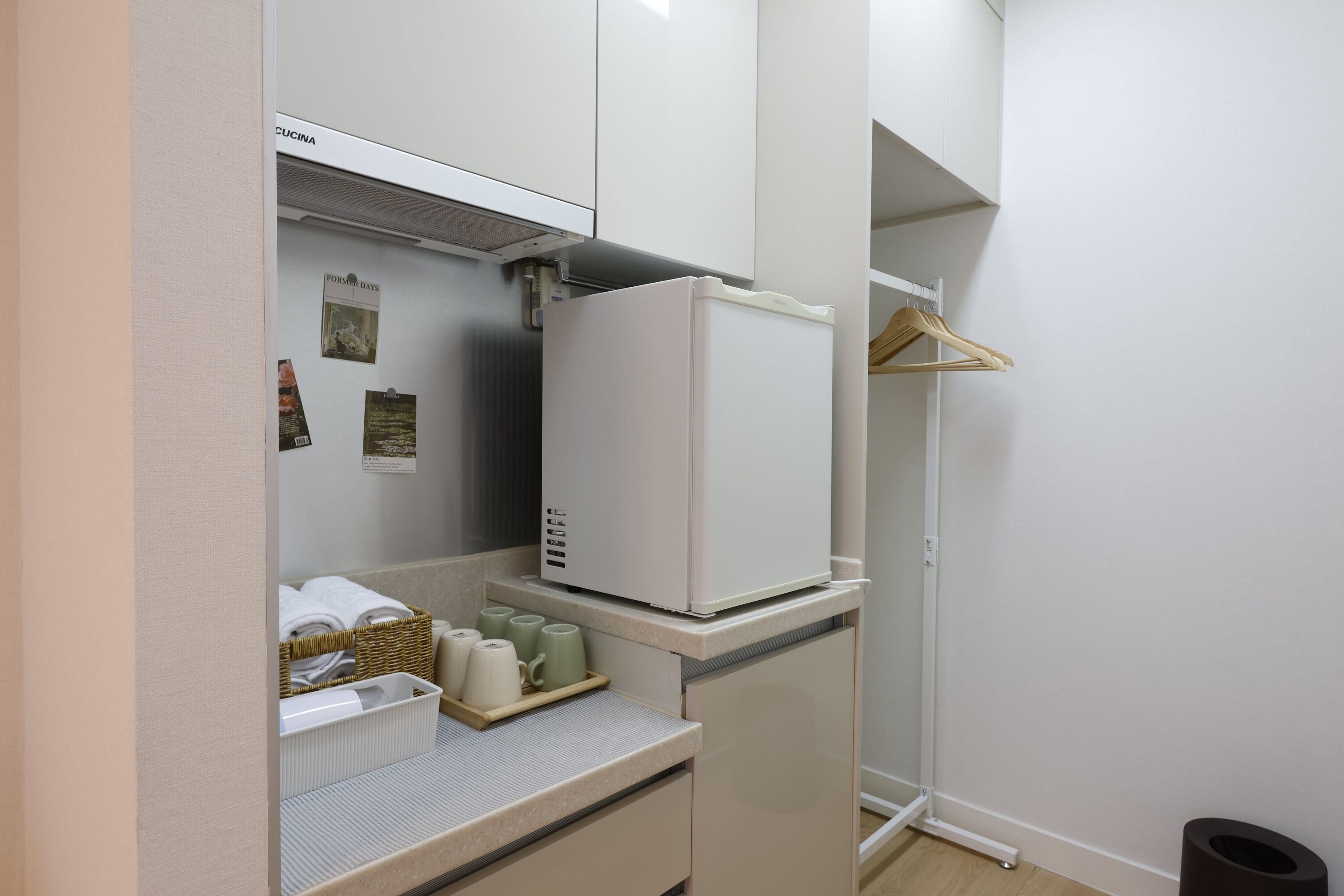 Eine kleine K üchenzeile mit einem weißen Kühlschrank, einer kompakten Arbeitsplatte und einem Korbkörbchen mit Handtüchern.