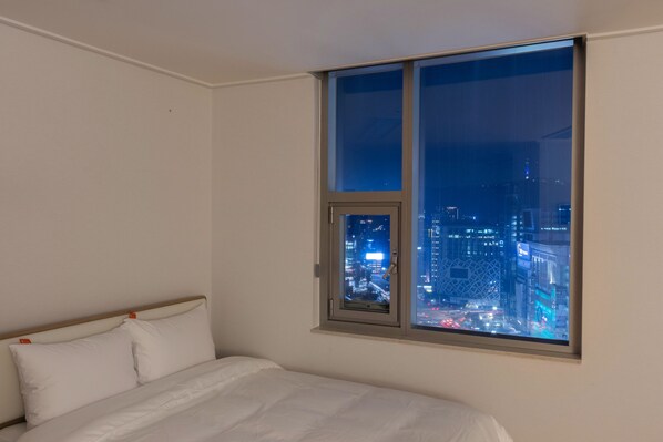 Un dormitorio con un ventanal grande que da a un paisaje urbano de noche.