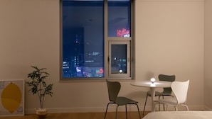 Una habitación con un ventanal grande, una planta en maceta, una mesa con dos sillas y una cama.