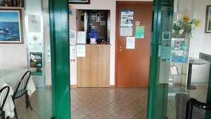 A hotel reception area with a wooden counter, framed artwork, and a menu board. - Hotel Giordana (Loano)