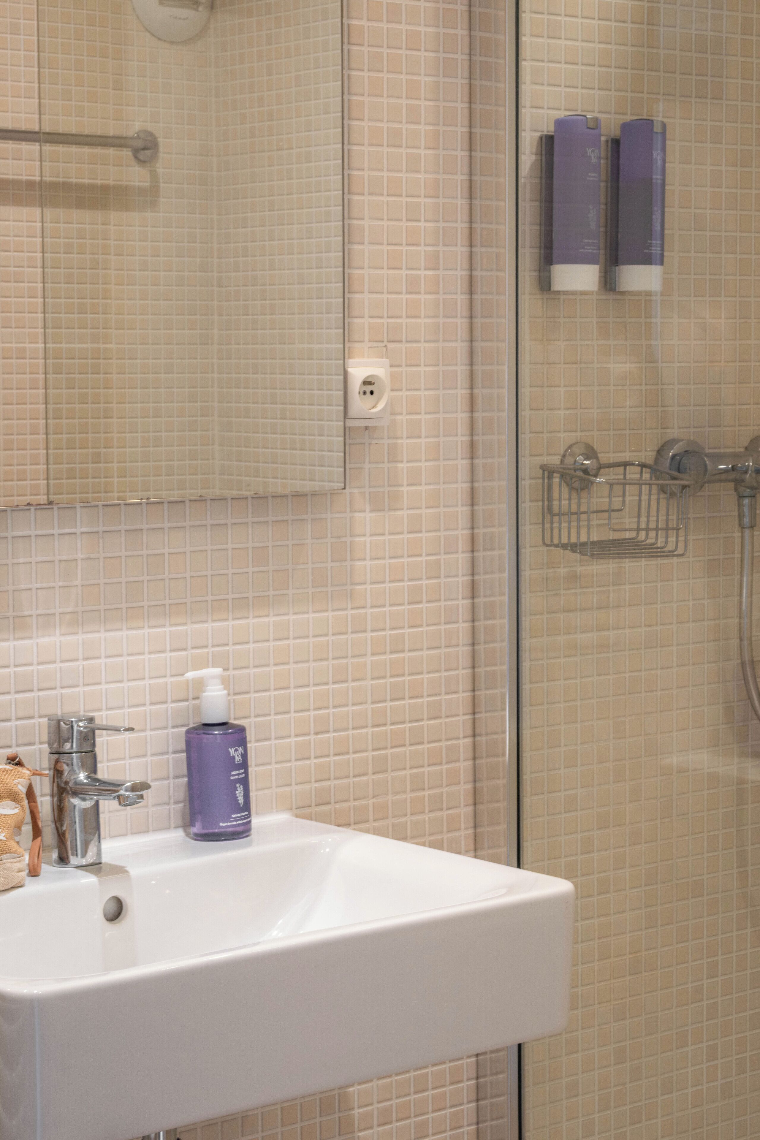 Un baño con lavamanos blanco, un espejo y zona de ducha.