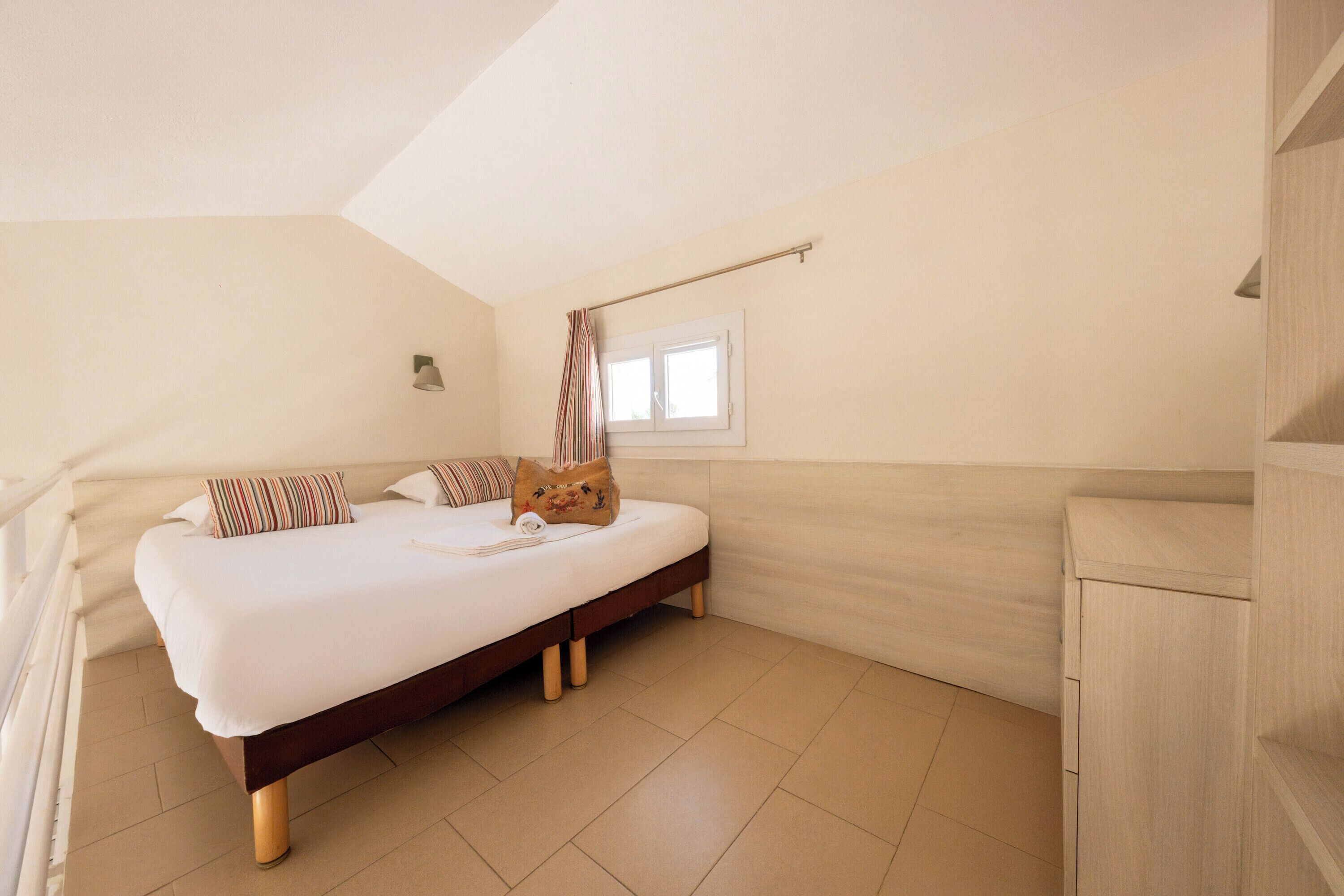 A bedroom with a bed, pillows, a window, and a wooden cabinet.