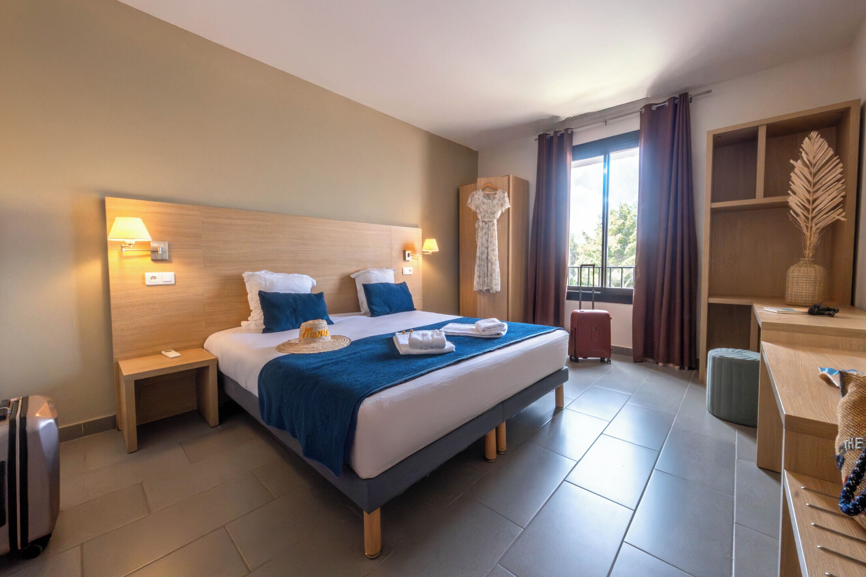 Een hotelkamer met een groot bed, twee nachtkastjes, een bureau en een raam met gordijnen.