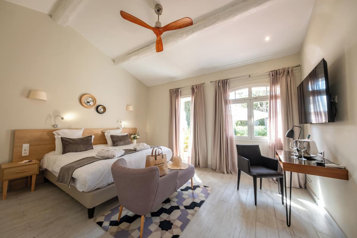 Ein modernes Hotelzimmer mit Bett, Schreibtisch, Sessel und Deckenventilator sowie einem Fernseher.