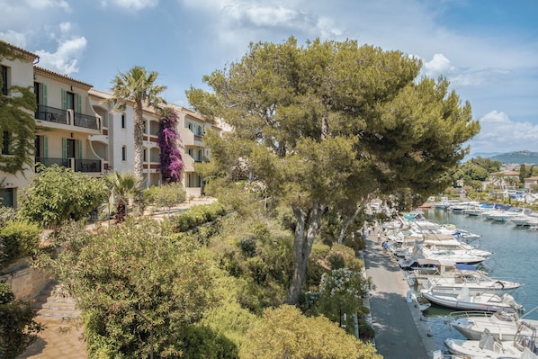 A marina with boats docked, a building with balconies, and a tree-lined pathway. - Appartements de l'Hélios - Îles des Embiez (Six-Fours-les-Plages)