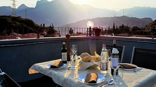 Mesa lista para una comida con vistas a la montaña, una botella de vino y una cesta de pan.