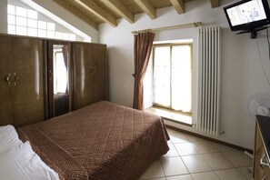 A bedroom with a bed, wardrobe, window with curtains, radiator, and a TV on the wall. - Hotel Doria (Nago-Torbole)