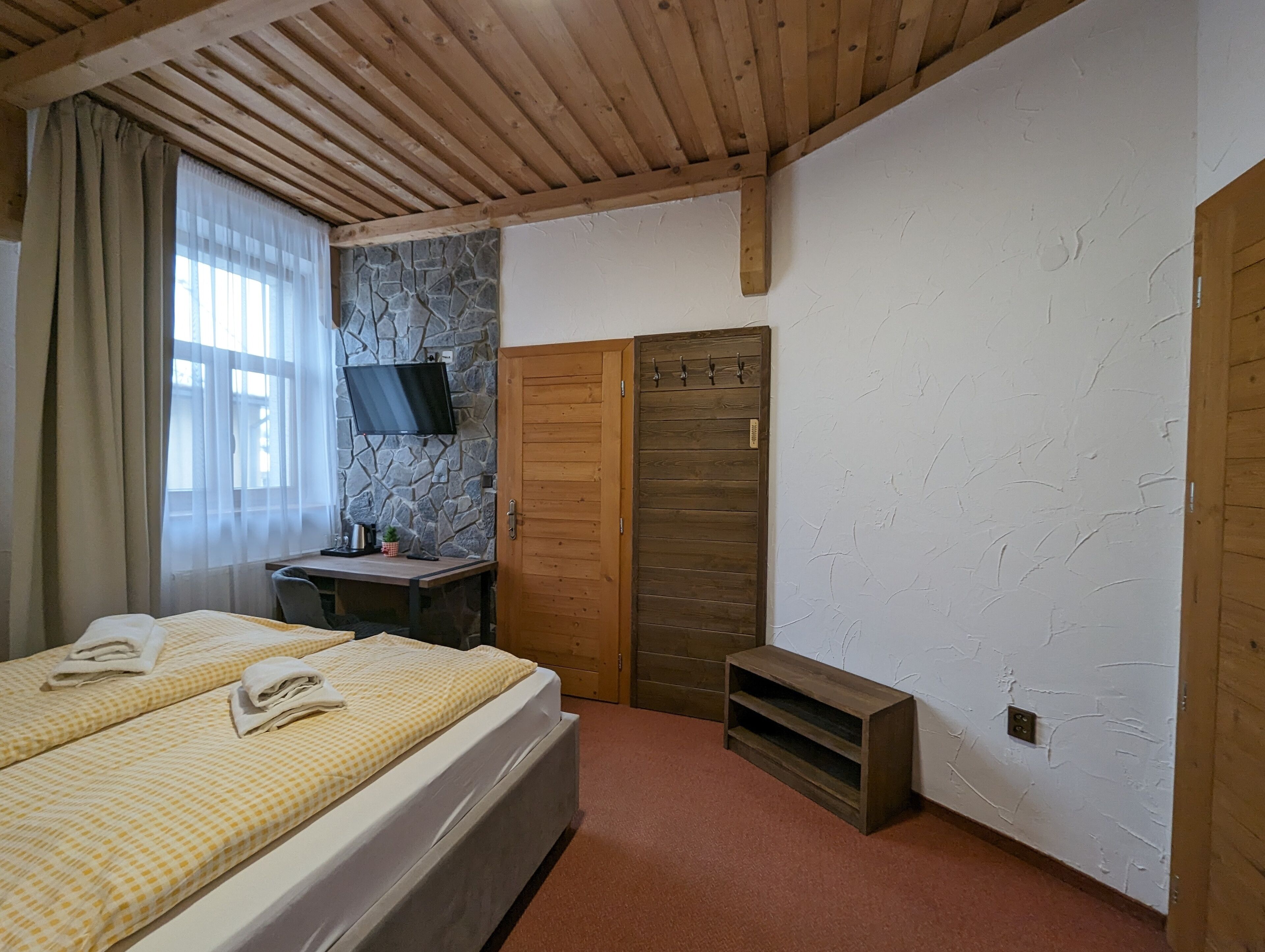 Un dormitorio con cama, escritorio, televisor y pared de piedra.