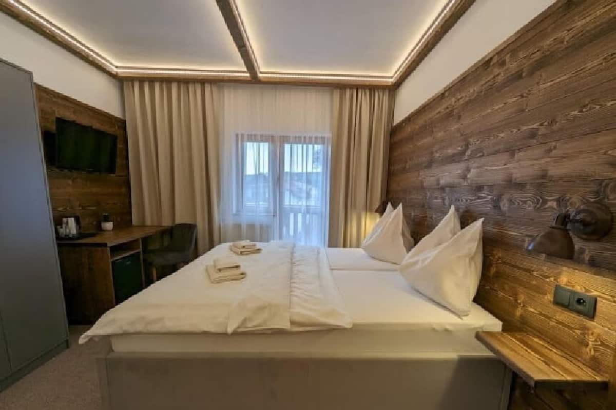 A hotel room with a large bed, wooden paneling on one wall, a desk with a chair, and a television on the wall.