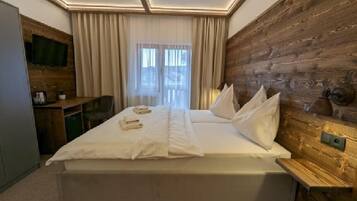 A hotel room with a large bed, wooden paneling on one wall, a desk with a chair, and a television on the wall.