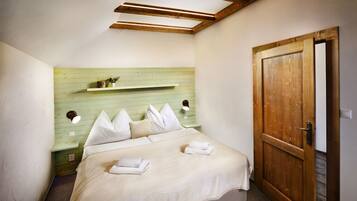 A bedroom with a bed, pillows, a nightstand, a shelf with decorative items, and a wooden door.