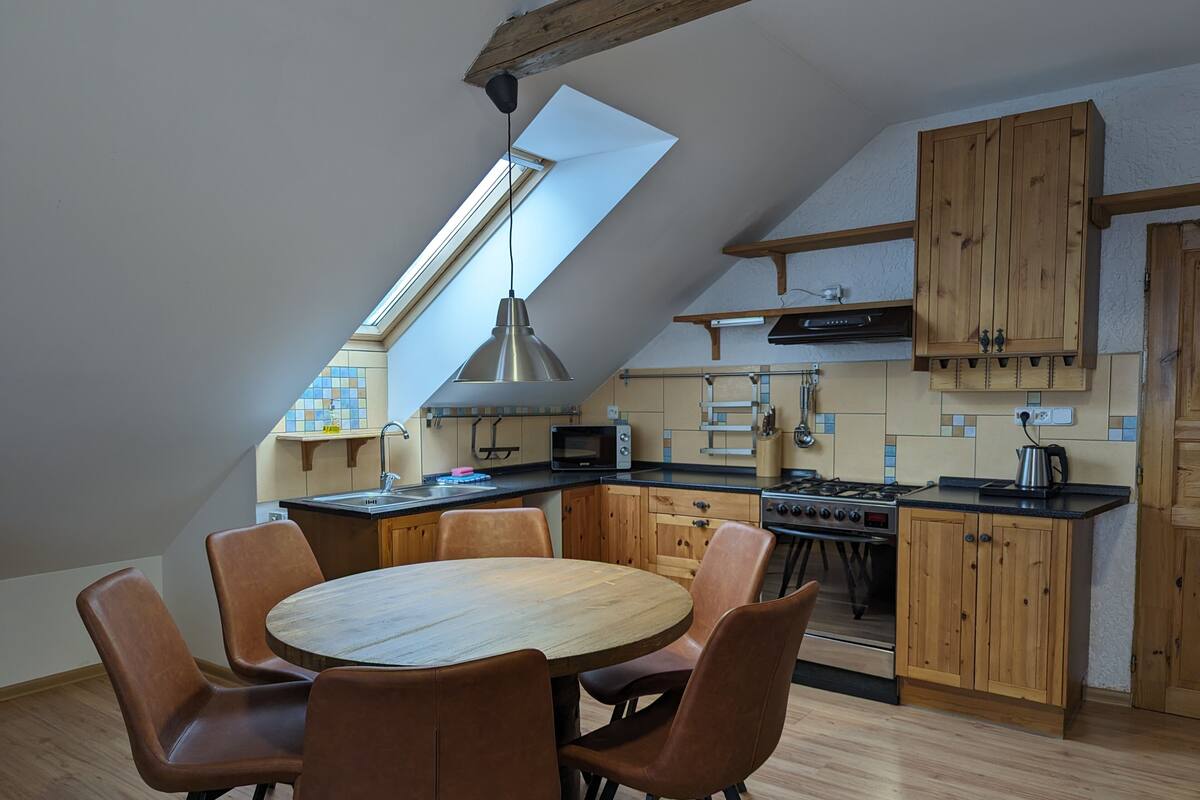 A modern kitchen with a skylight, wooden cabinets, and a dining area with brown chairs.