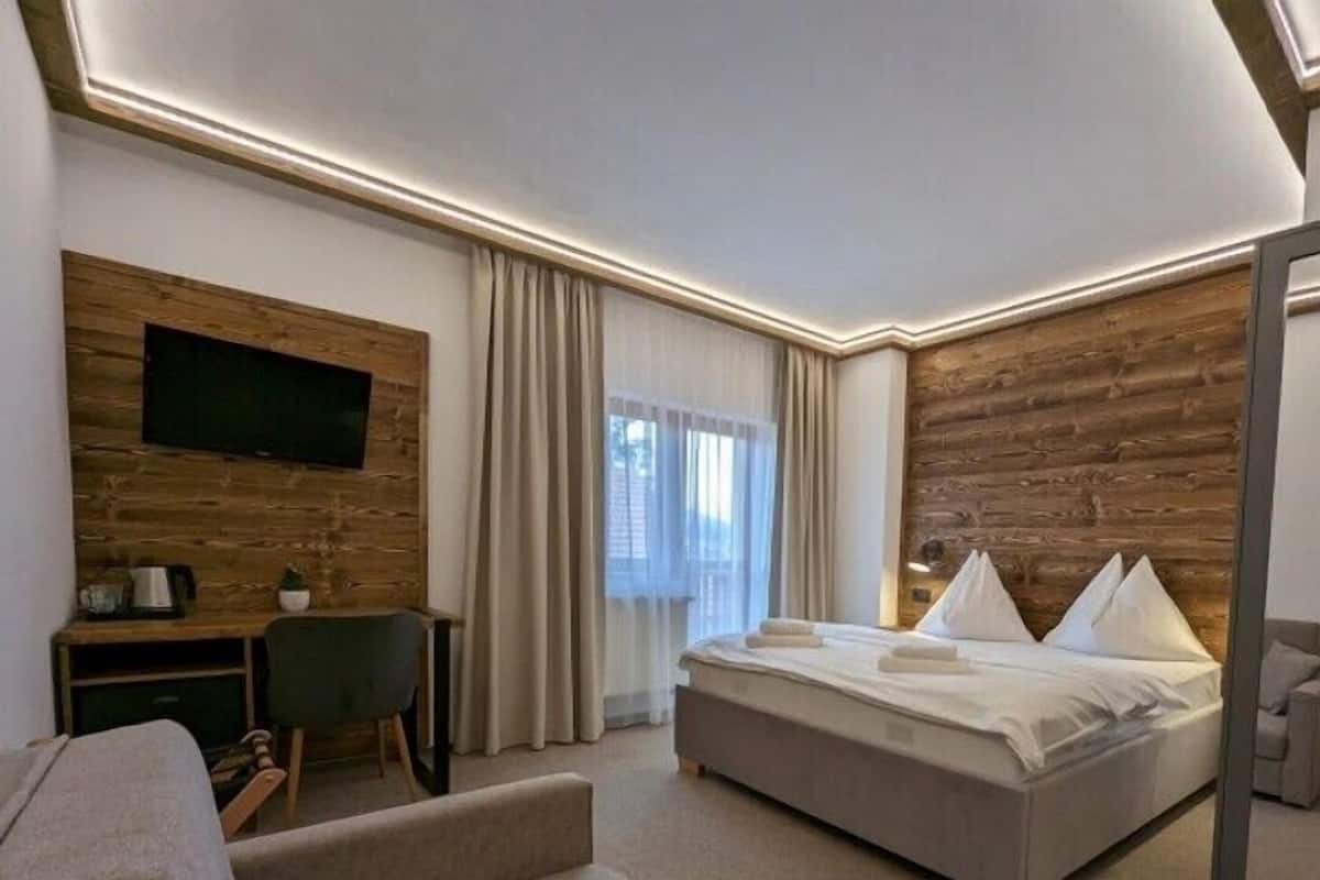 A modern hotel room with a wooden accent wall, a large bed, a desk with a chair, and a television mounted on the wall.