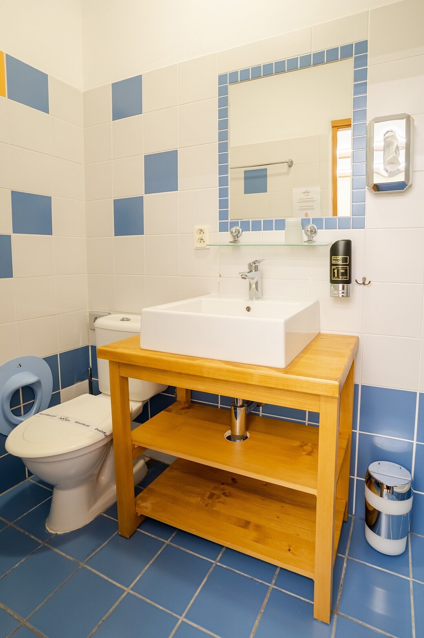 A bathroom with a white sink, wooden vanity, blue and white tiled walls, a toilet, and a hand dryer.