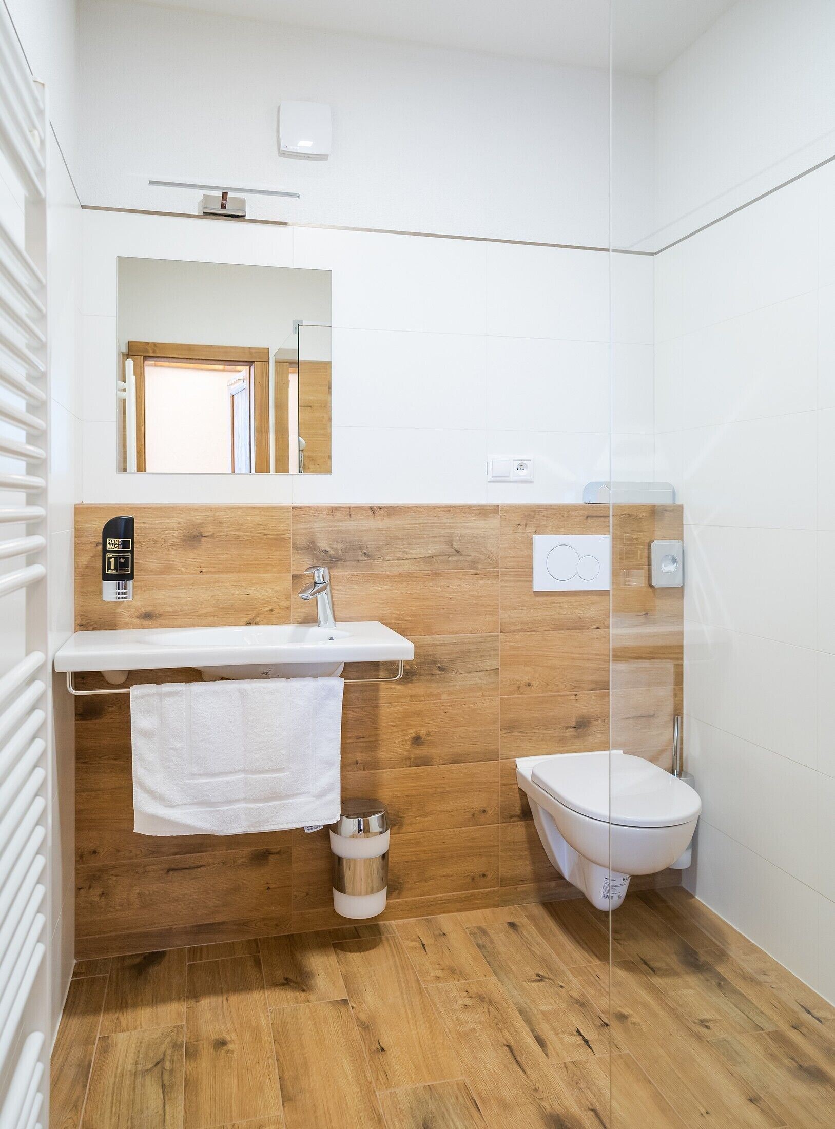 A bathroom with a wooden vanity, a white sink, a toilet, and a mirror.