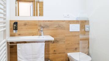 A bathroom with a wooden vanity, a white sink, a toilet, and a mirror.