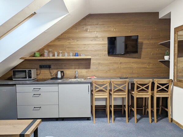 Cocina compacta con pared de madera, televisor de pantalla plana, microondas y pileta. Hay cuatro sillas de madera y una mesita.