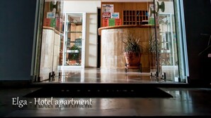 The entrance to Elga Hotel Apartment with a clear glass facade, a neon sign above the entrance, and a potted plant inside. - Elga Hotel (Kos)