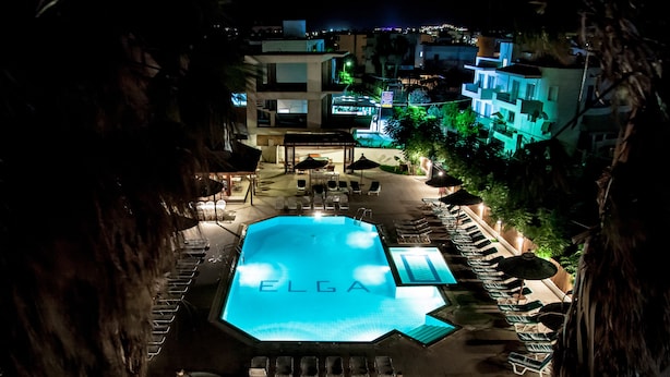 A nighttime view of a hotel with a swimming pool, lounge chairs, and a well-lit outdoor area. - Elga Hotel (Kos)