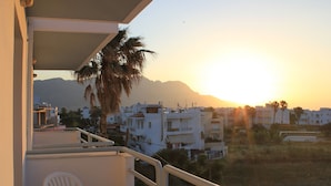 A balcony with a white chair and a table, overlooking a residential area with buildings and a mountain in the background. - Elga Hotel (Kos)