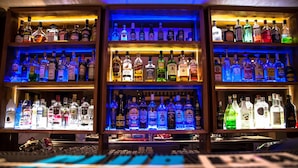 A bar with shelves of various liquor bottles, illuminated by colored lighting. - Elga Hotel (Kos)