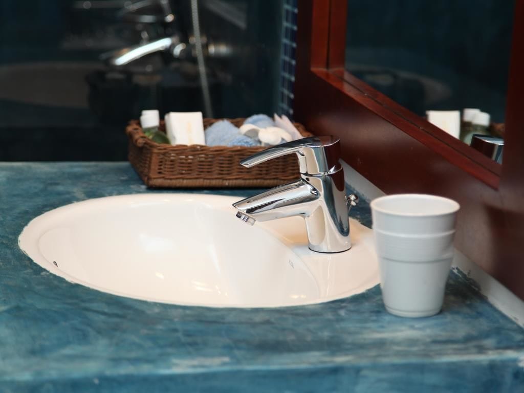 Un lavamanos con grifo cromado, una taza blanca y una cesta de mimbre con artículos de tocador.