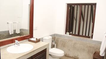 Un baño con un lavamanos blanco, un espejo, un inodoro y una ventana con marco de madera.