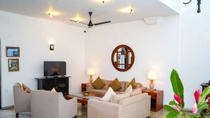 Una sala de estar moderna con un sofá, sillones, una mesa de centro, un televisor y un ventilador de techo.