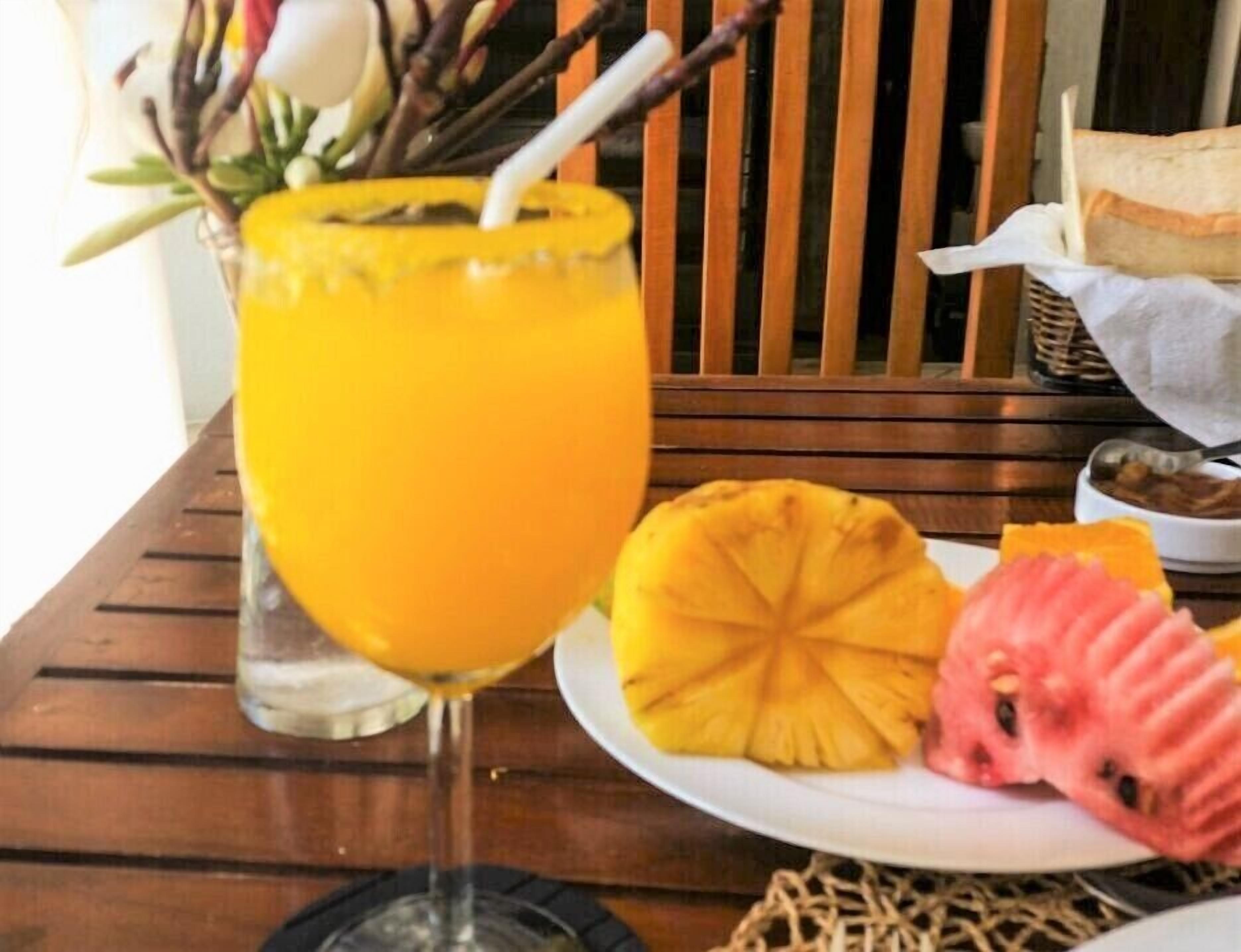 Un verre de jus d’orange, une tranche d’ananas et une tranche de pastèque sur une table en bois.