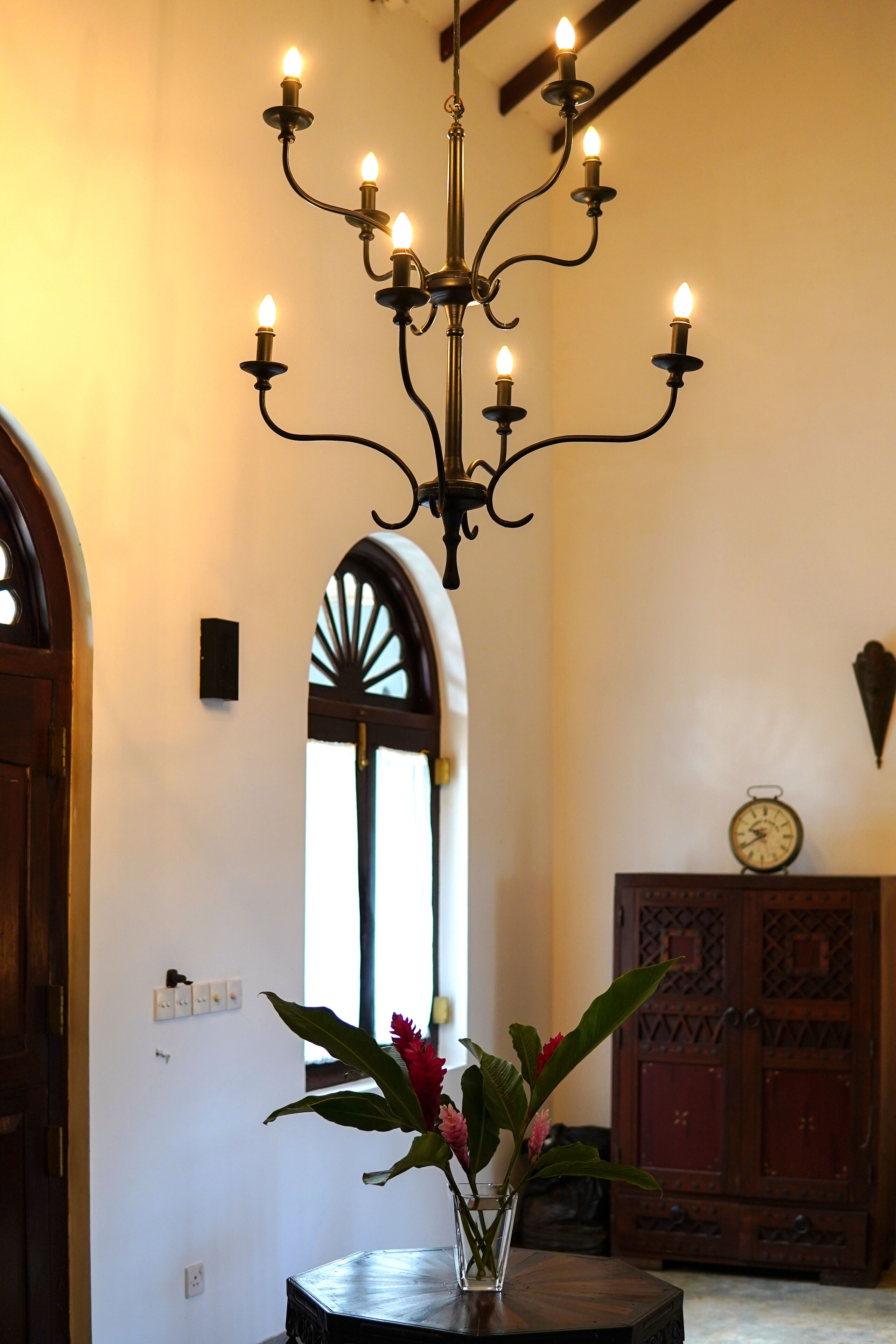 A chandelier with multiple lights, a wooden cabinet, and a vase with flowers in a hallway.