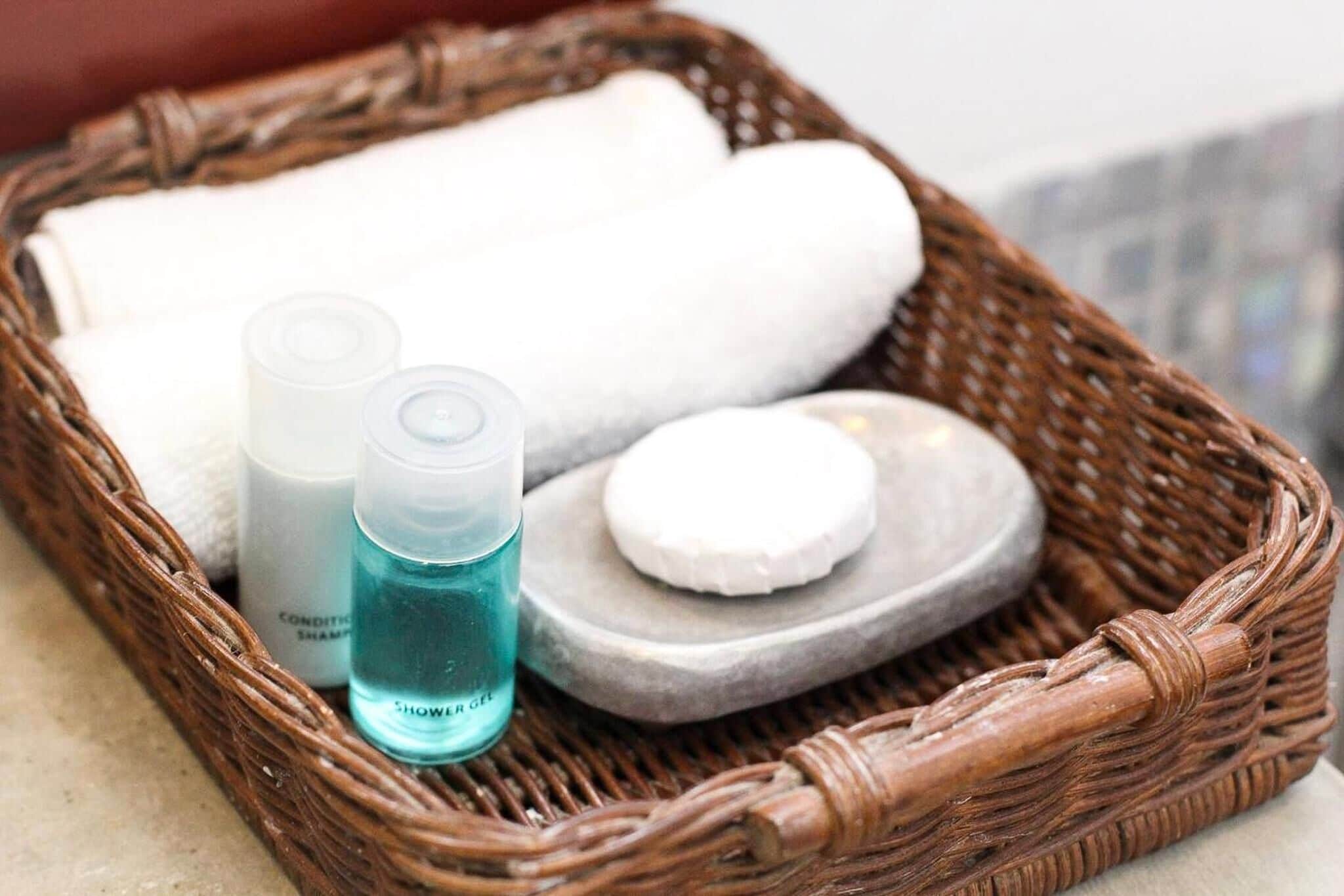 Un panier en osier contenant une serviette blanche, deux flacons de gel douche et un savon.