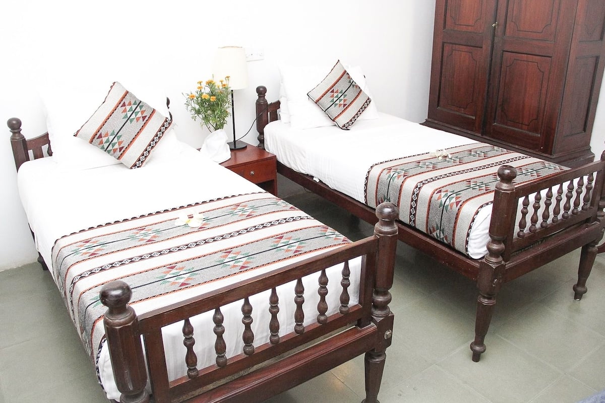 Dos camas de madera con cubrecamas estampados, una mesita de noche con lámpara y un armario.