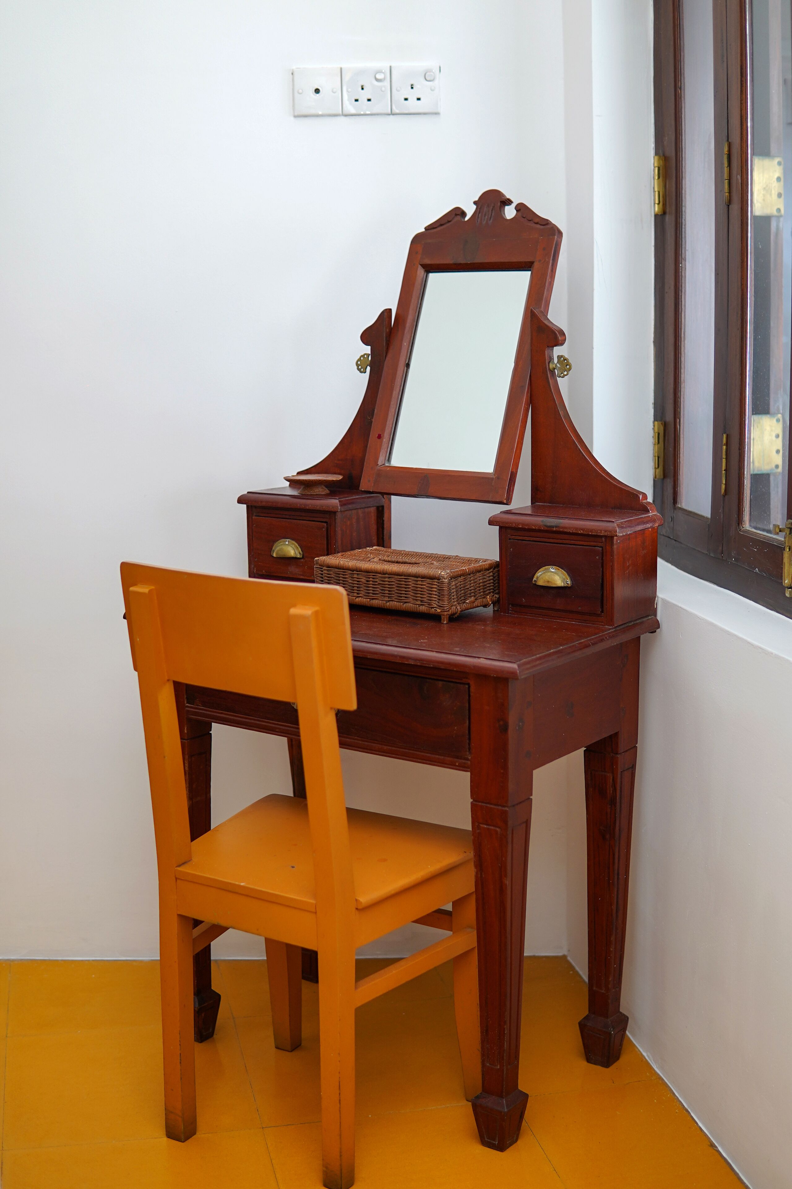 A wooden desk with a mirror, a chair, and a small basket.