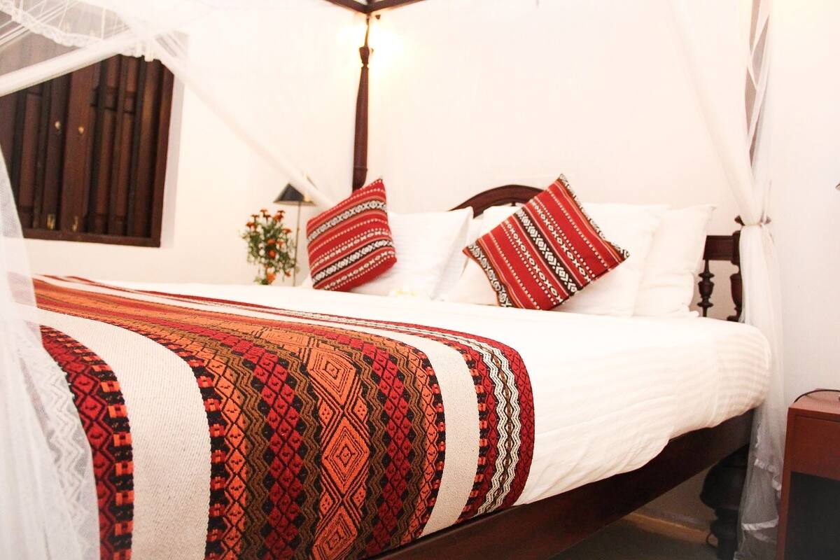 Una cama con dosel, almohadas estampadas y una manta decorativa.