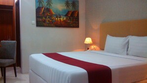 A hotel room with a bed, a chair, a painting of a tropical scene, and a nightstand with a lamp. - Sarila Hotel Sukoharjo (Sukoharjo)