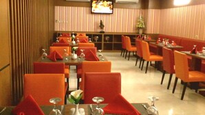 A restaurant with striped wallpaper, orange chairs, and tables set with red napkins and glassware. - Sarila Hotel Sukoharjo (Sukoharjo)