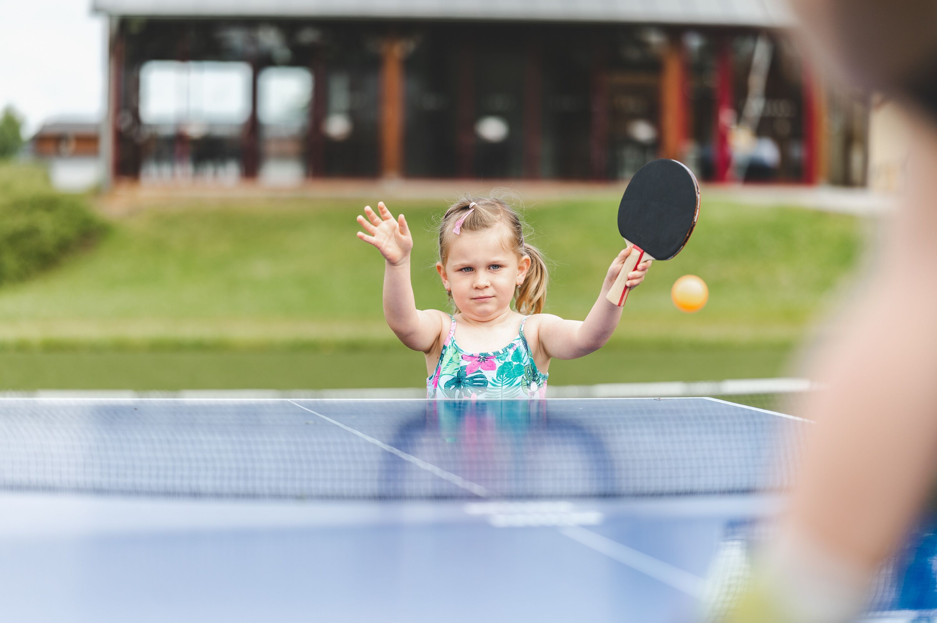 A child playing table tennis outdoors with a net in front of a building with columns.