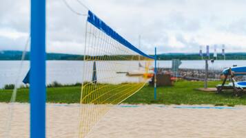 Enjoy a game of volleyball on the beach with a net set up on the sandy area overlooking the calm body of water.