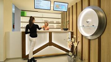 Una recepción con interior de madera, una planta en maceta y dos monitores mostrando información.
