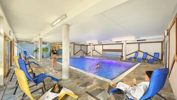 An indoor swimming pool with blue chairs and a person swimming.