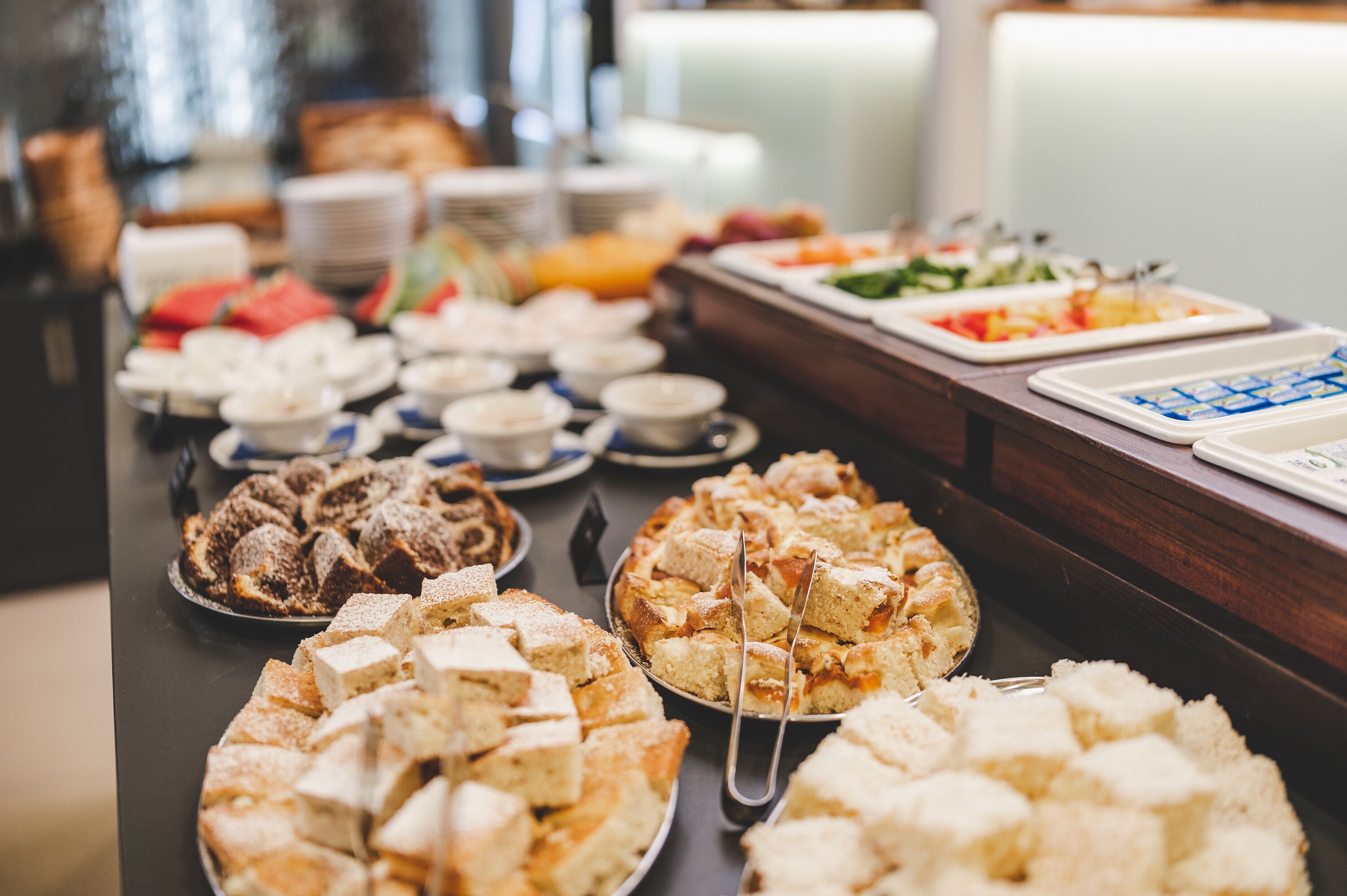 A buffet table with various food items including cakes, pastries, and fruits.