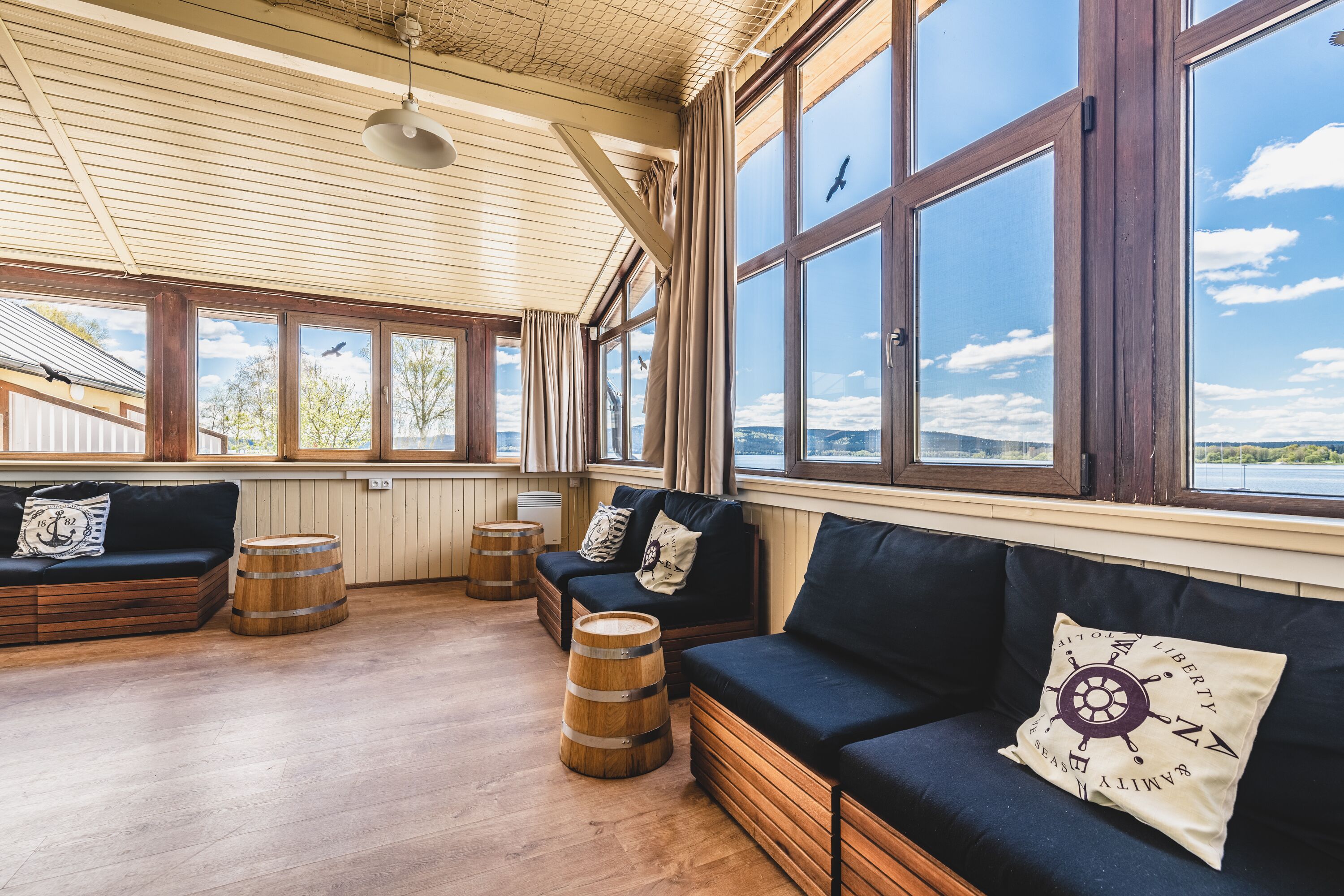 A spacious room with large windows, wooden floors, and a dark blue sofa with nautical-themed pillows.
