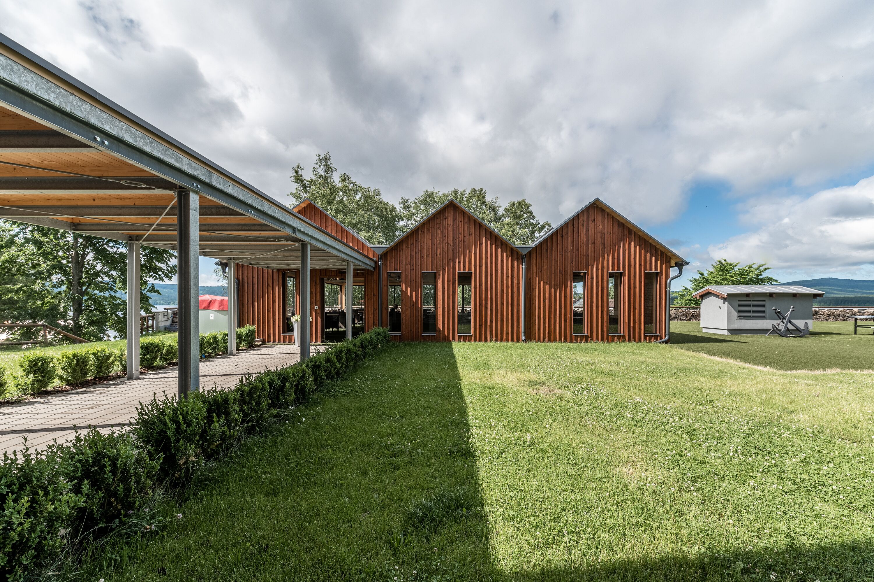 A modern wooden cabin with a covered patio, a grassy lawn, and a view of the sea.