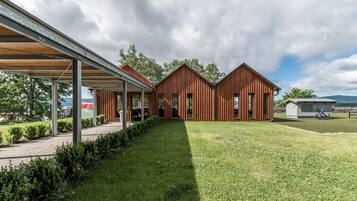 A modern wooden cabin with a covered patio, a grassy lawn, and a view of the sea.