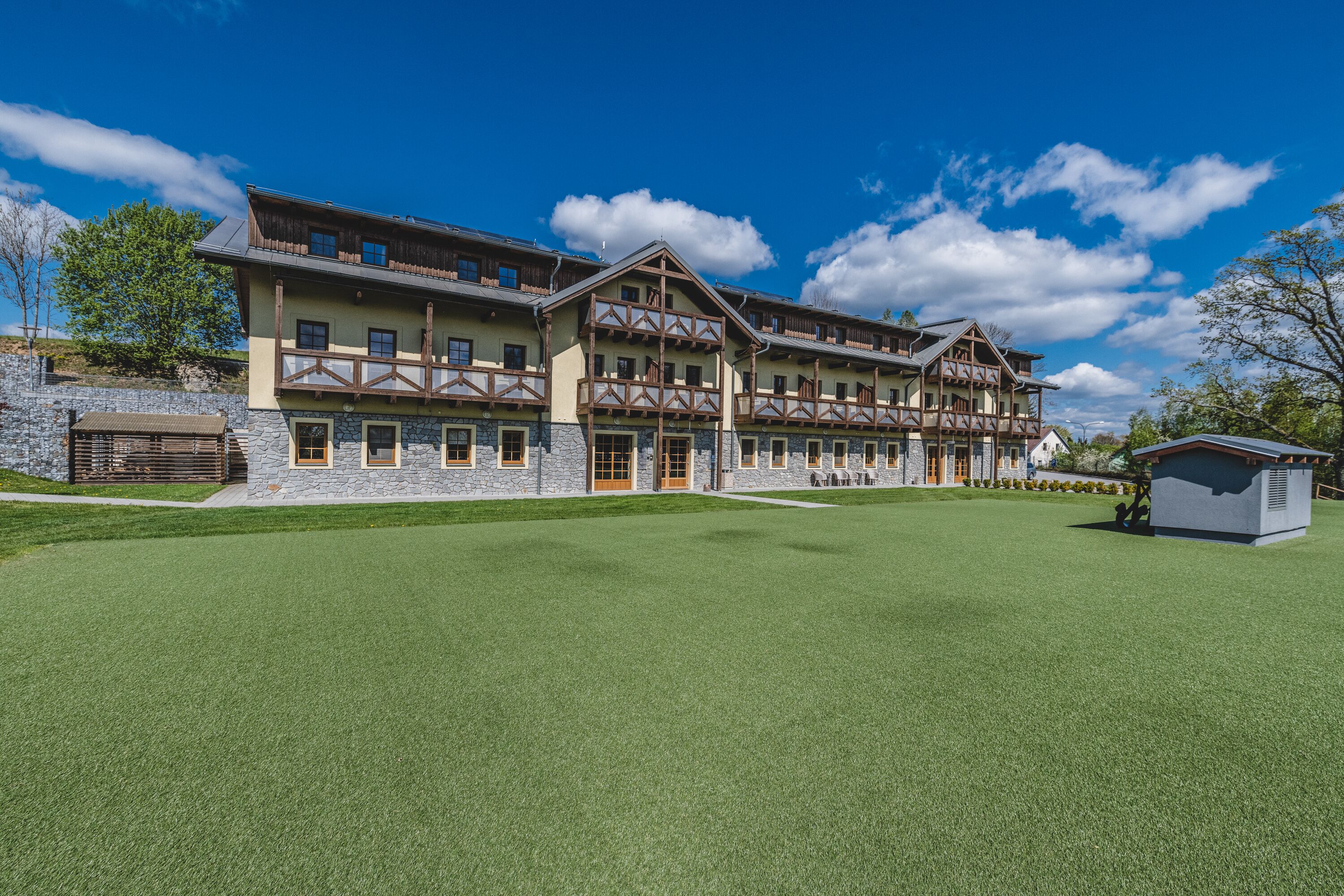 A large, multi-story building with a stone facade and wooden balconies, surrounded by a well-maintained lawn.