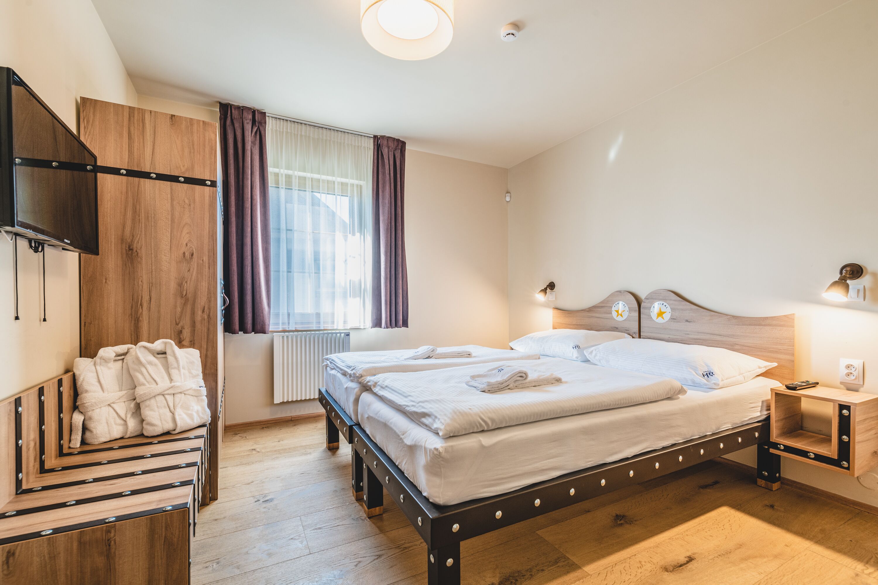 A bedroom with a bed, a wooden wardrobe, a bedside table with a lamp, and a window with curtains.