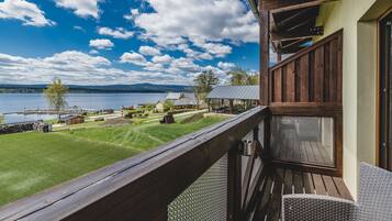 A balcony with a view of a lake, a grassy area, and a building in the background.